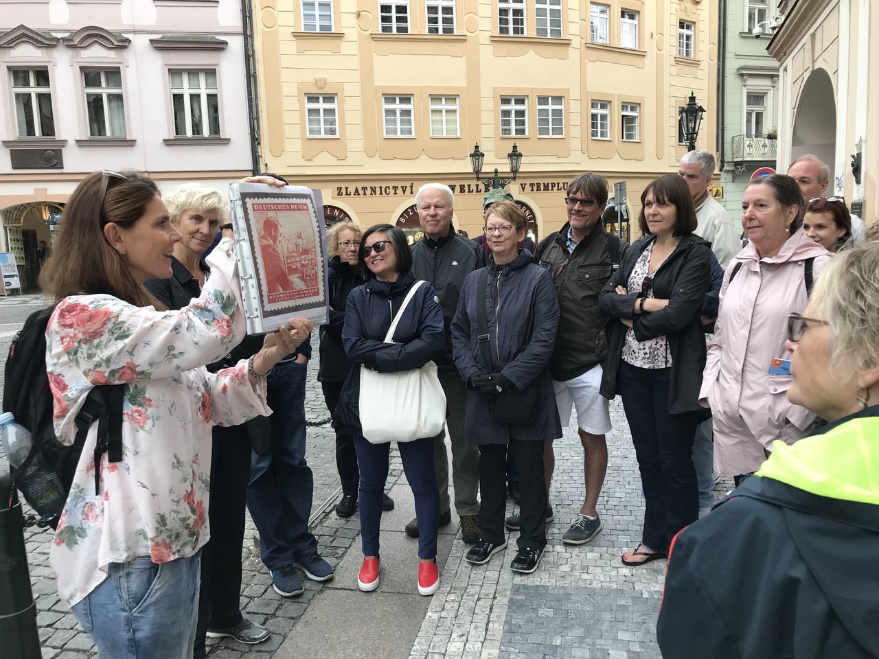 A woman speaks up and shows a picture of Prague's history to a group of people