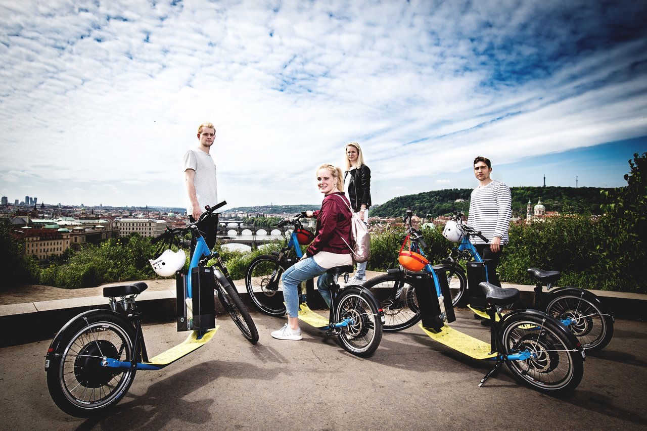 4 people on and around an electric scooter, with a view of the city