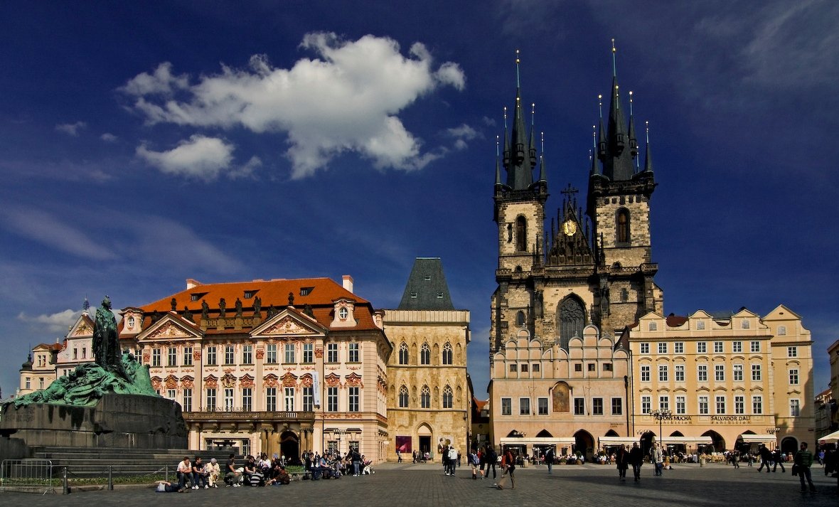 A large square, bustling with passersby and dominated by the palace and the church under a blue sky.