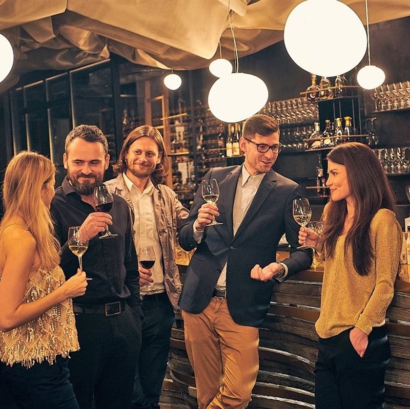 Two women and three men drinking a glass of wine and champagne at a bar