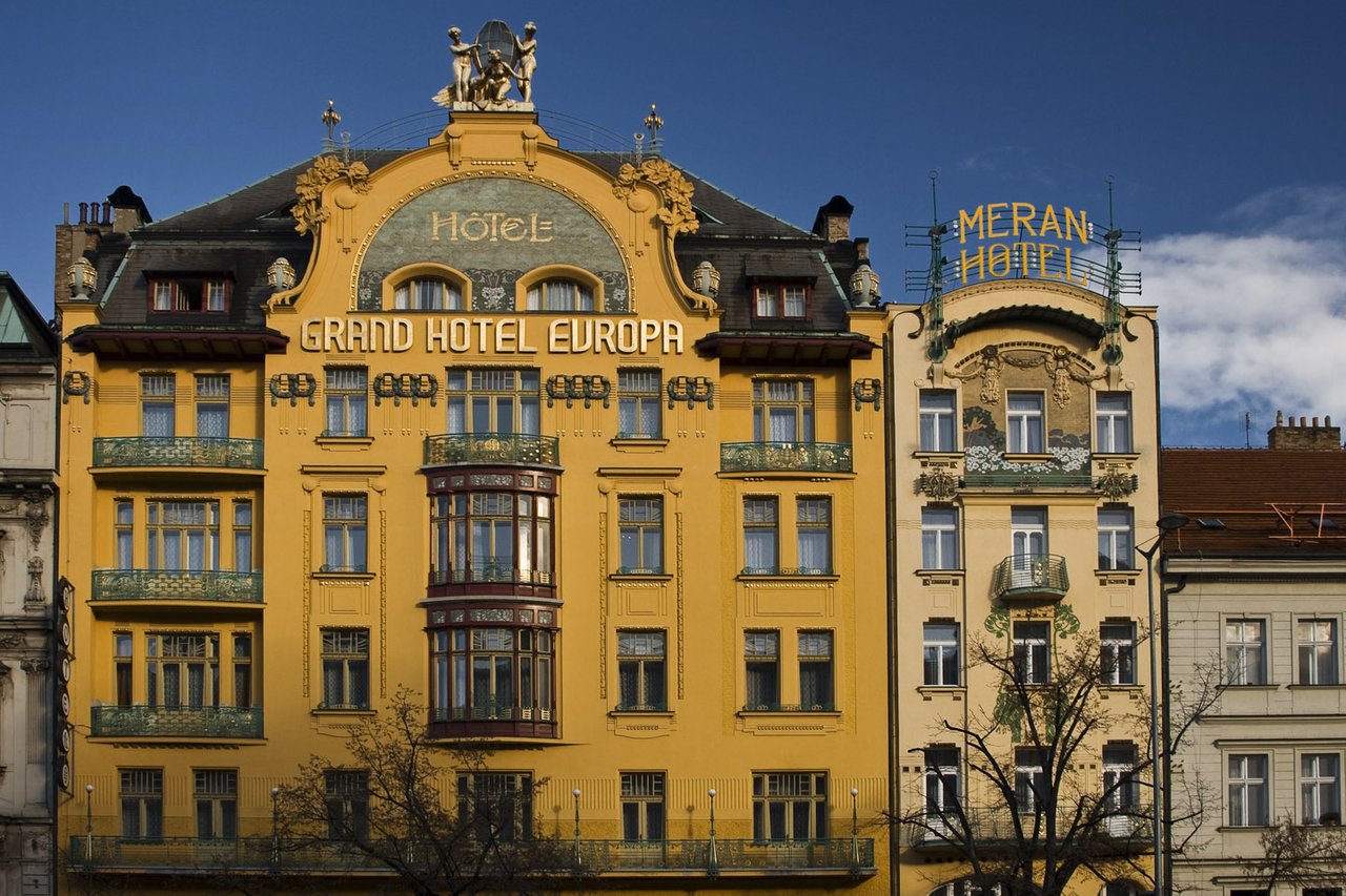 A large yellow facade adorned with moldings, featuring green balconies and the inscription “Grand Hôtel Europa” on the facade