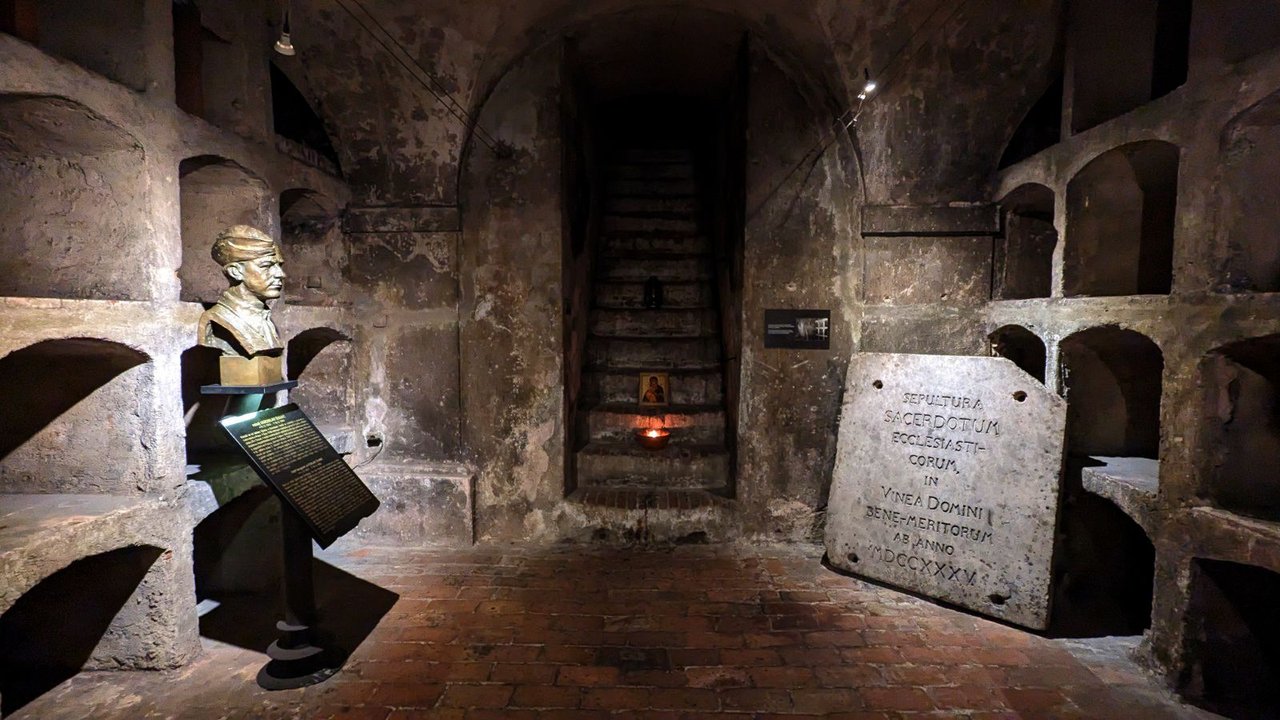 A dimly lit underground room, built of gray stone, containing a carved bust resting on a pedestal