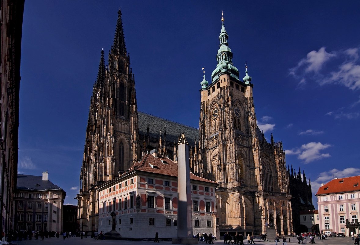 An imposing cathedral with facades adorned with stained-glass windows and carved details, and a tower topped by a turquoise dome