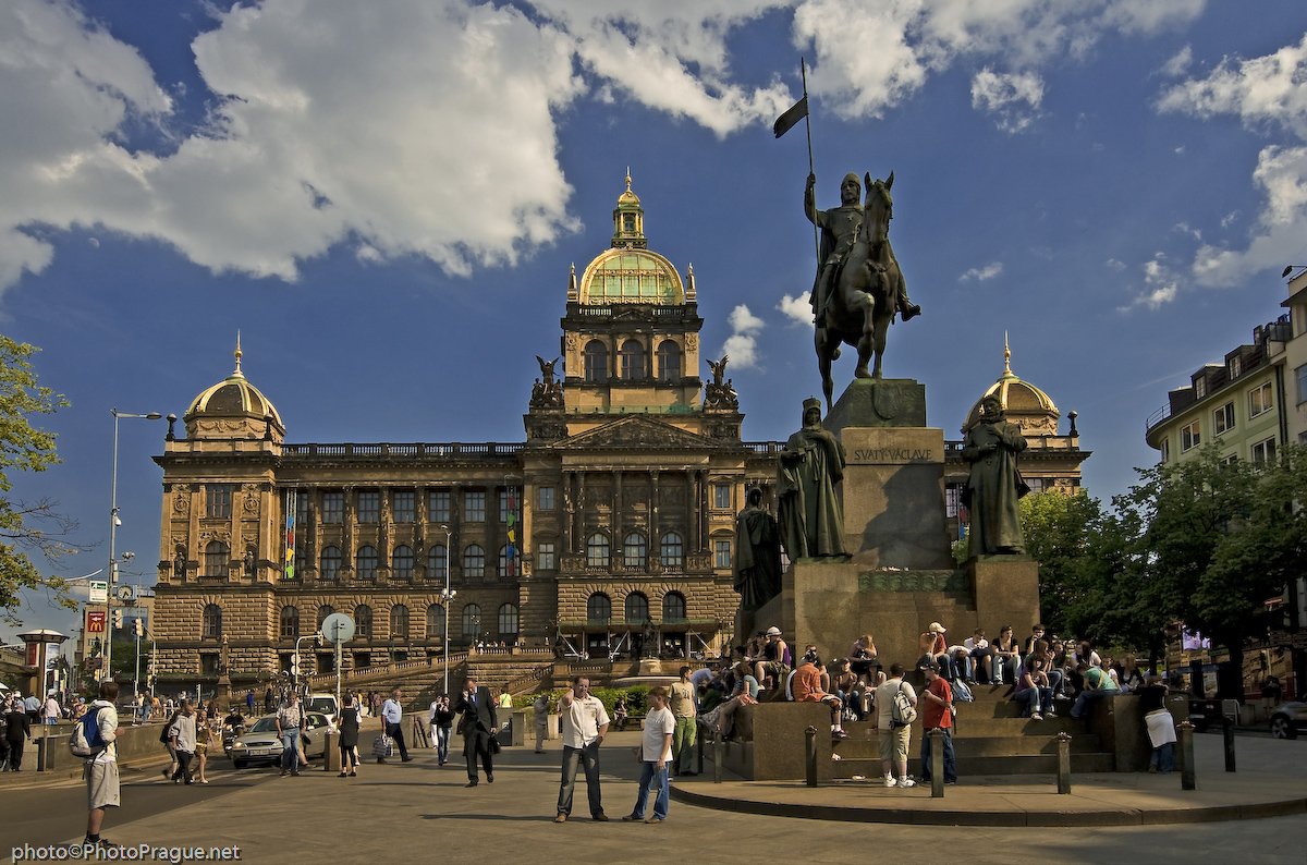 A large bronze statue of a man on horseback in a bustling square, in front of a huge stone palace with a golden dome